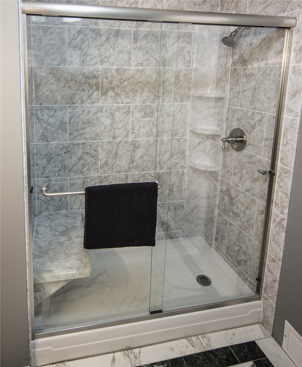 A modern shower with a glass door, featuring a neatly hung black towel on the side.