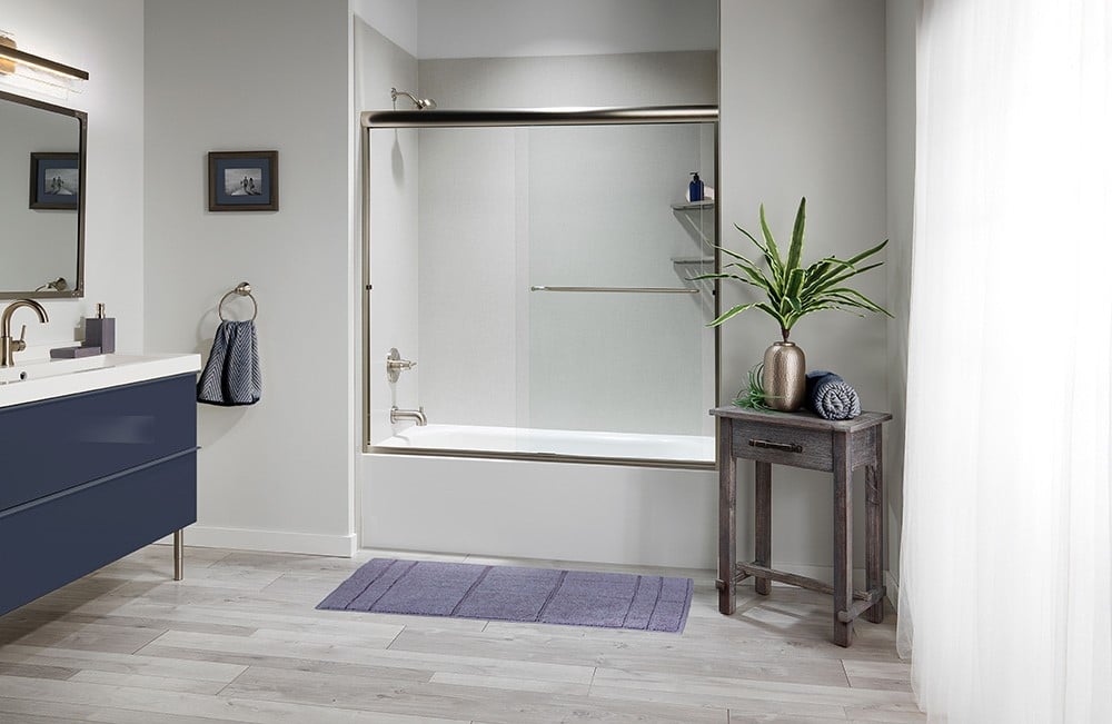 Modern bathroom with a bathtub and shower, navy vanity, purple bath mat, small table with plant, and large window with sheer curtain.