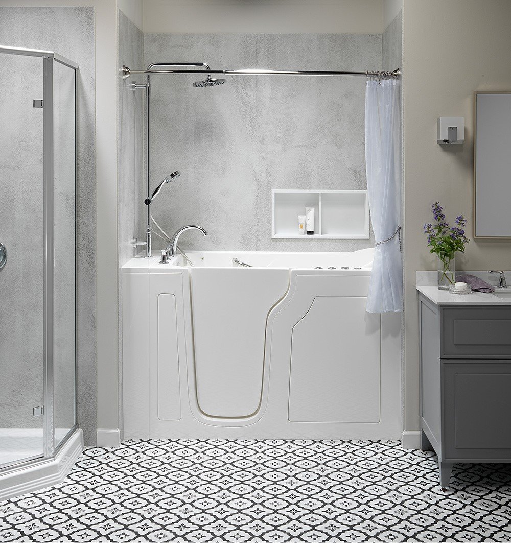 A modern bathroom with a white walk-in bathtub, gray textured walls, patterned tile flooring, and a glass shower enclosure.