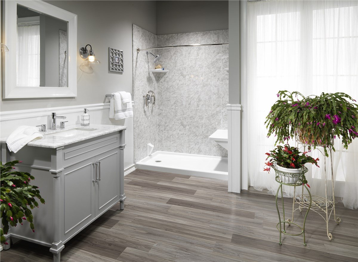 A modern bathroom with a gray vanity, marble shower wall, and decorative plant stands near a window.