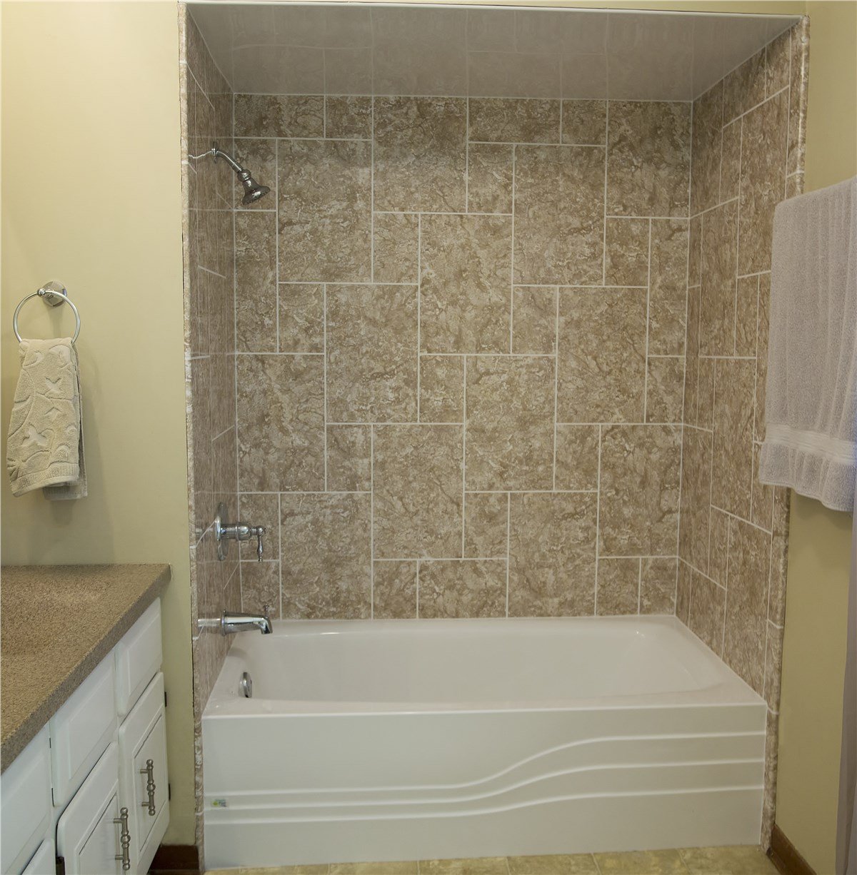A clean bathroom with a beige tiled bathtub, chrome fixtures, and white cabinetry with silver handles.