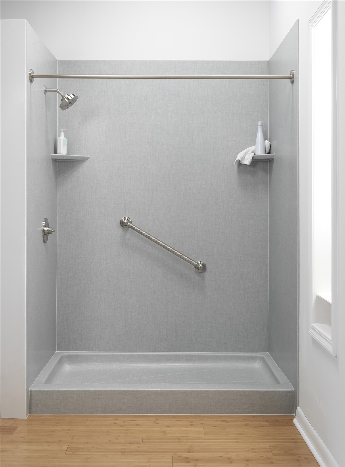 Minimalist walk-in shower with gray walls, grab bar, and corner shelves holding toiletries.