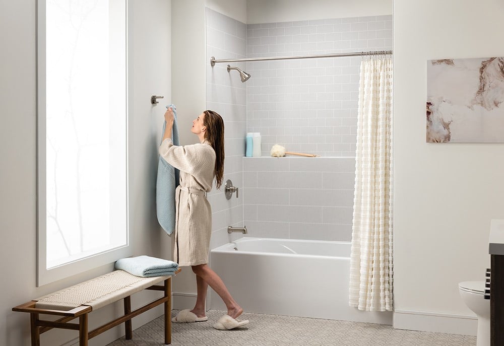 A minimalist bathroom with a woman in a bathrobe hanging a blue towel beside a white bathtub.