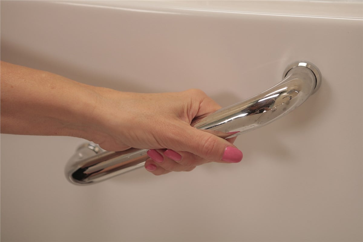 A close-up of a hand gripping a chrome safety bar attached to the side of a white walk-in bathtub.