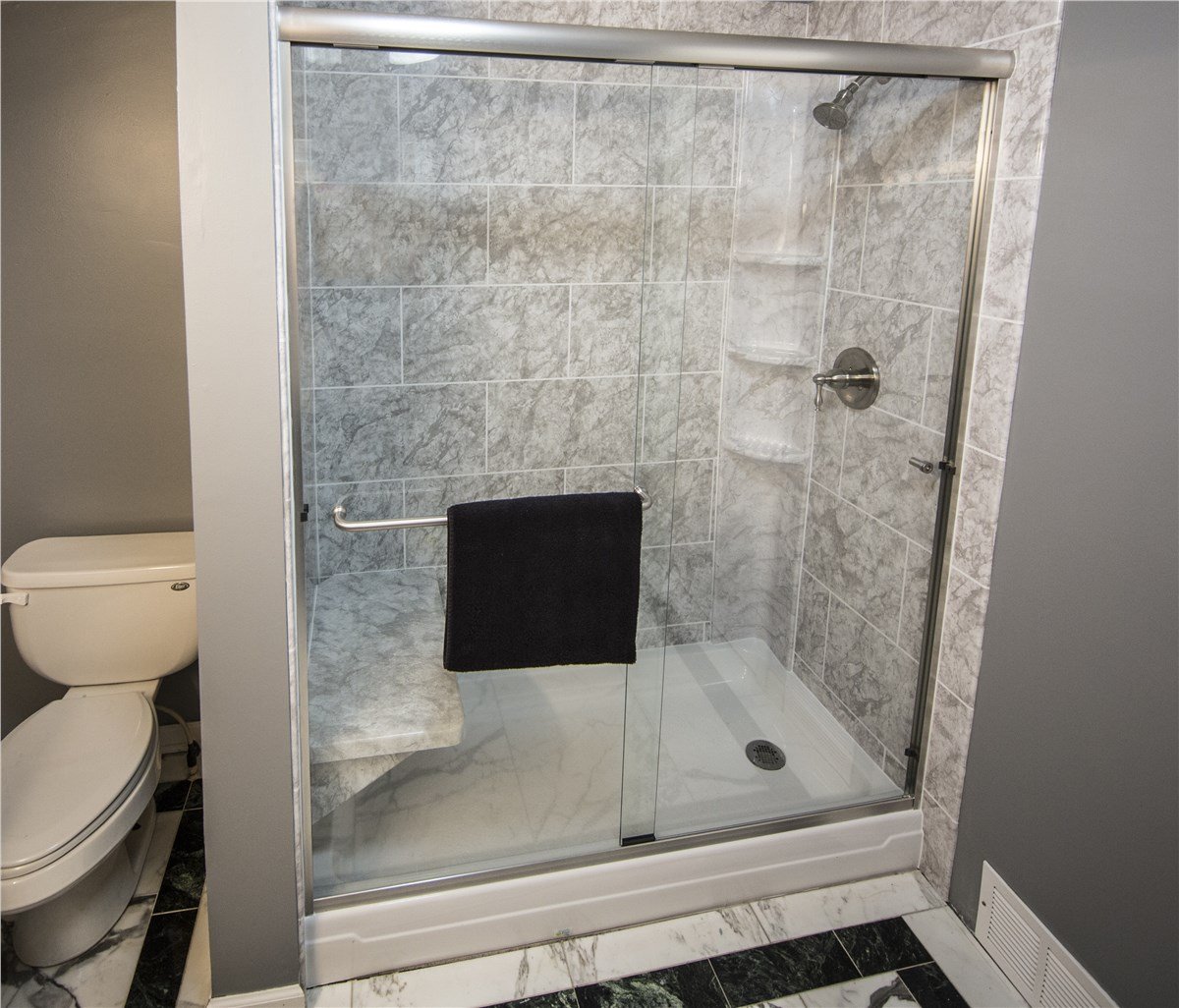 A modern bathroom with a marble-tiled walk-in shower, built-in bench, and adjacent toilet.